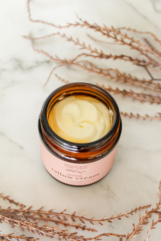 Open jar of Renew Tallow Cream on white marble with dried copper branches, whipped tallow visible inside
