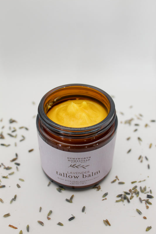 Open jar of Lavender Tallow Balm showing the golden whipped balm inside, scattered with dried lavender buds