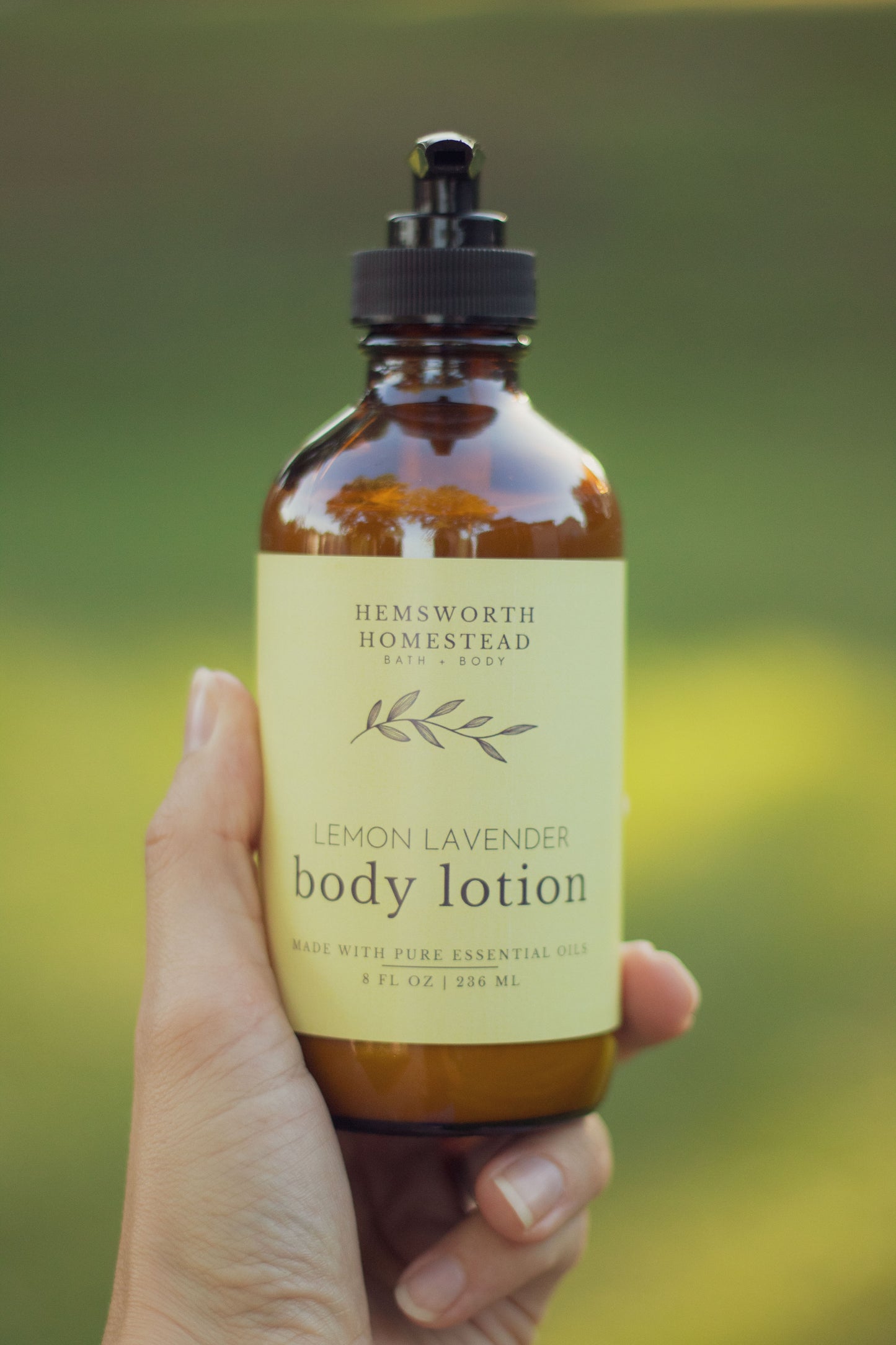 Hand holding a bottle of Lemon Lavender body lotion with a pale yellow label, outdoors in the grass