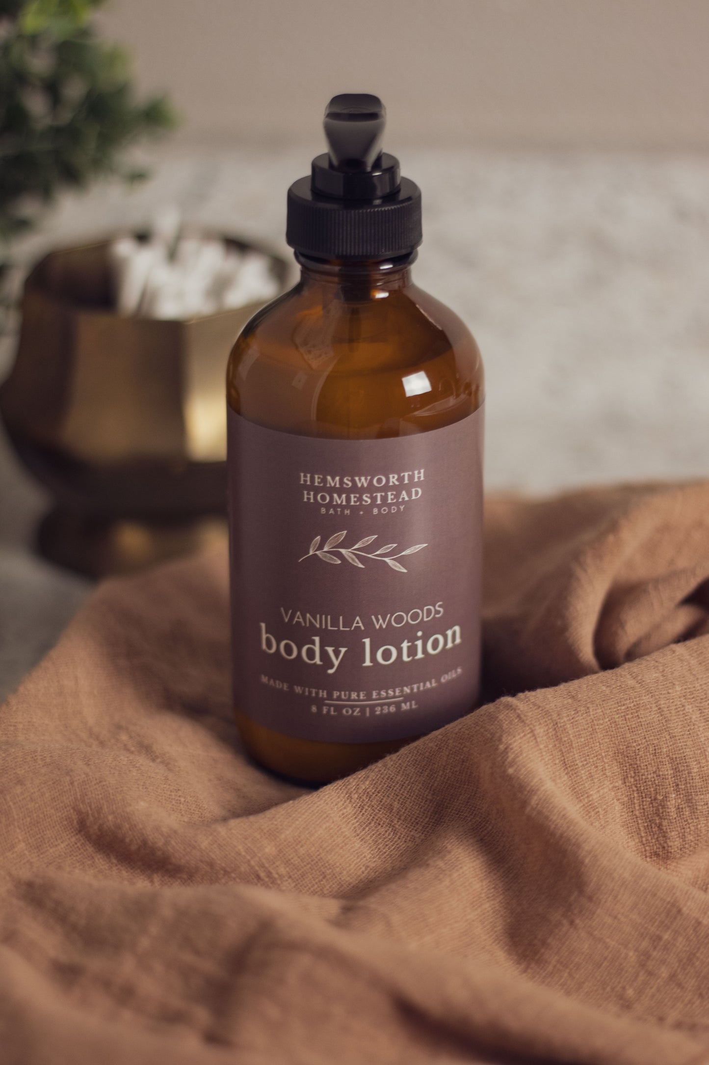 Vanilla Woods body lotion bottle resting on a draped tan fabric background
