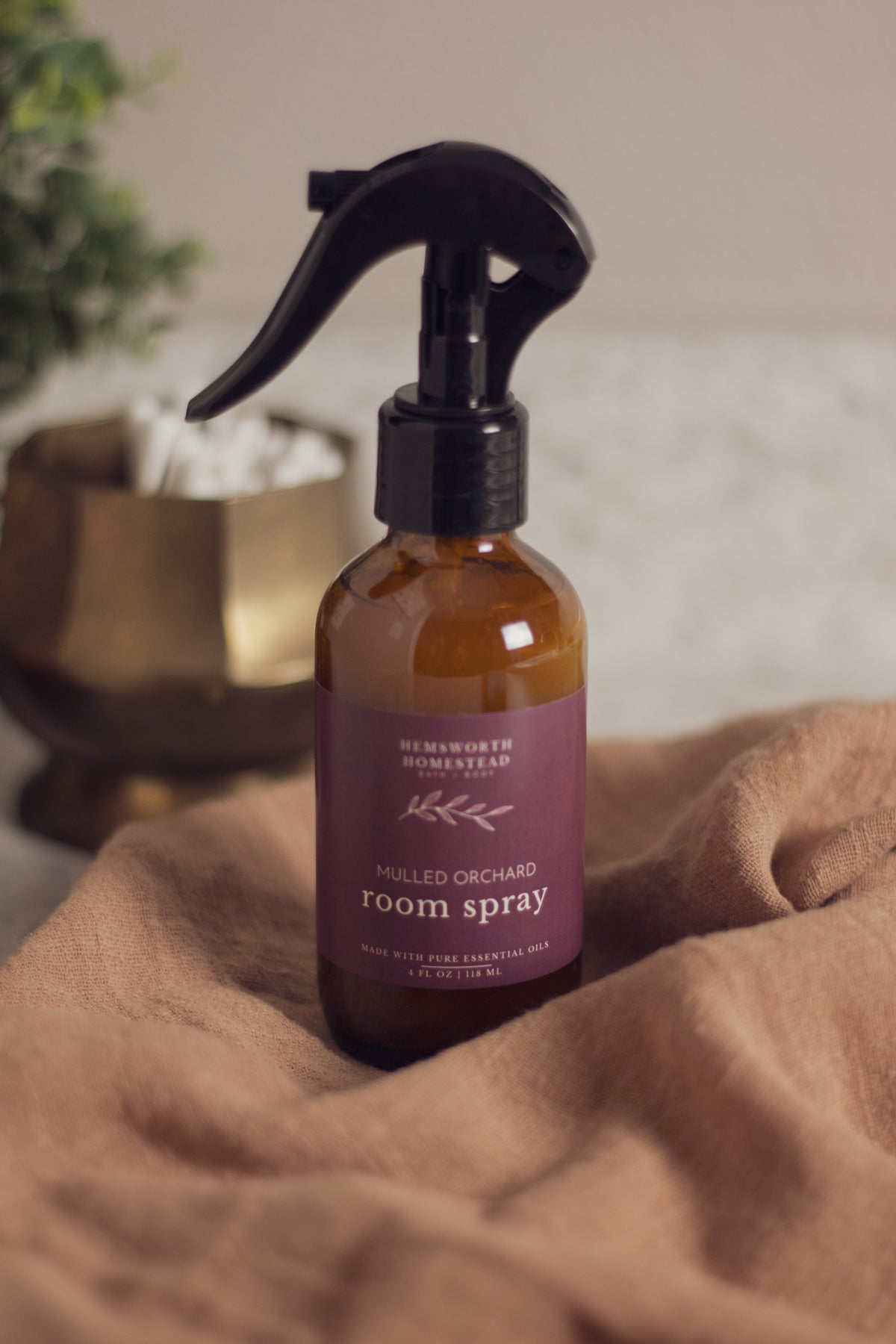 Mulled Orchard room spray bottle resting on a draped tan fabric background