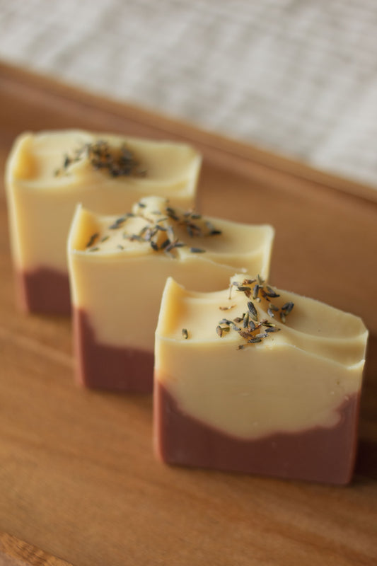 Three bars of Lemon + Lavender soap lined up on a wooden tray, each topped with dried lavender