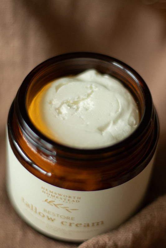 Open amber jar of Restore Tallow Cream showing the white whipped cream inside, on tan linen