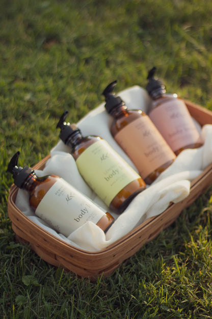 Four bottles of natural body lotion nestled in a picnic basket with a cream cloth, sitting on green grass