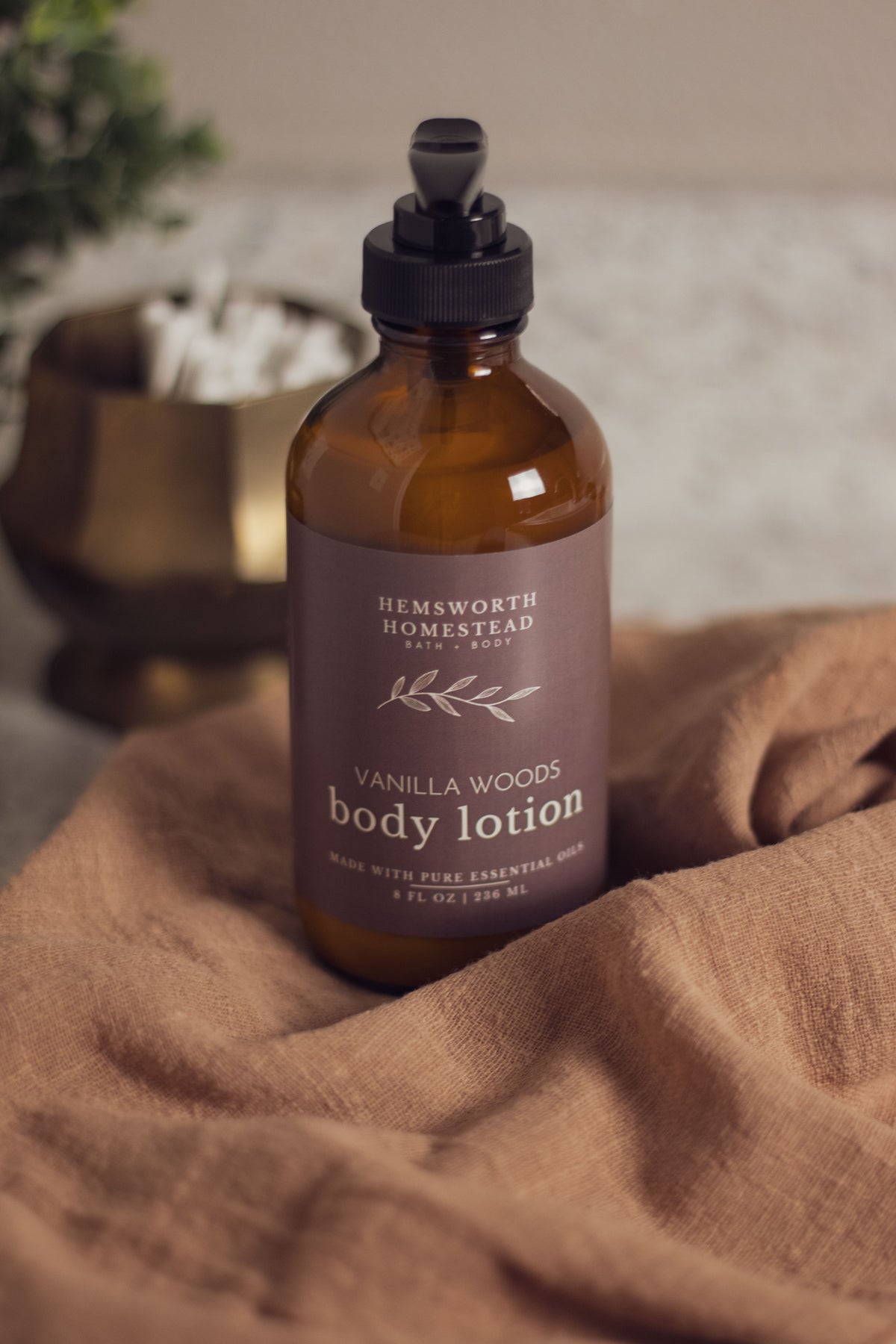 Vanilla Woods body lotion bottle resting on a draped tan fabric background