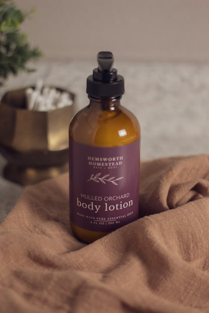 Mulled Orchard body lotion bottle resting on a draped tan fabric background