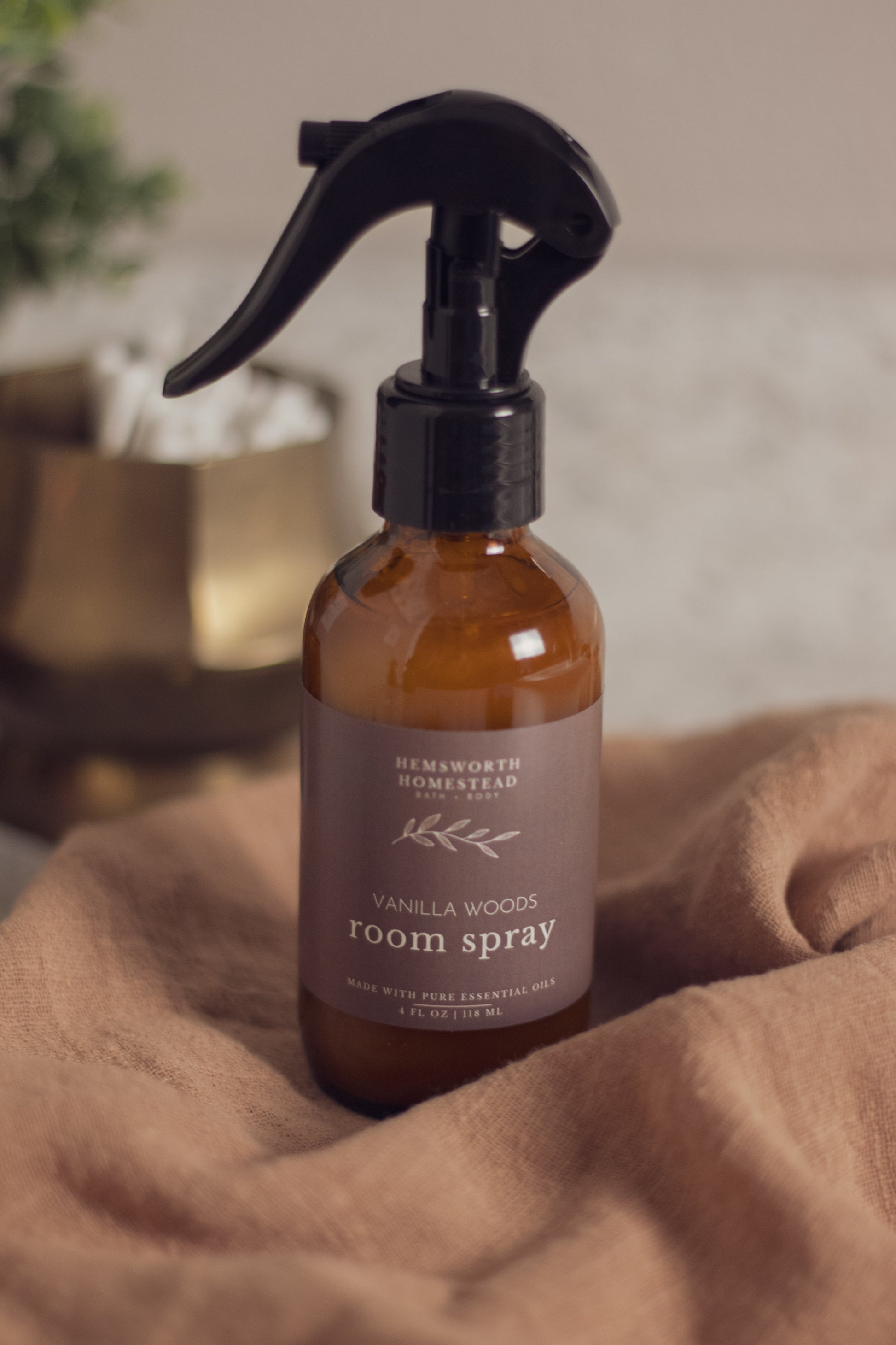 Vanilla Woods room spray bottle resting on a draped tan fabric background