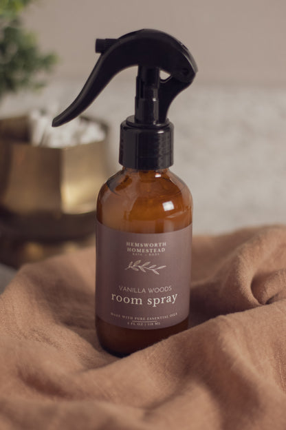 Vanilla Woods room spray bottle resting on a draped tan fabric background