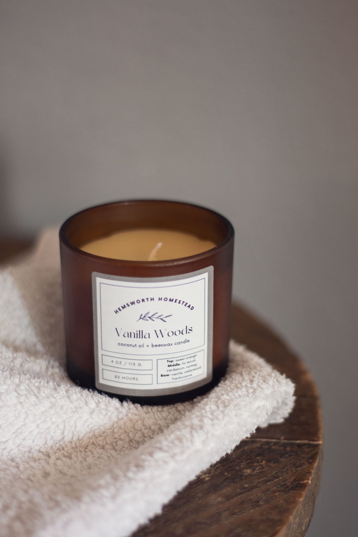 Vanilla Woods candle on a folded white towel atop a wooden stool