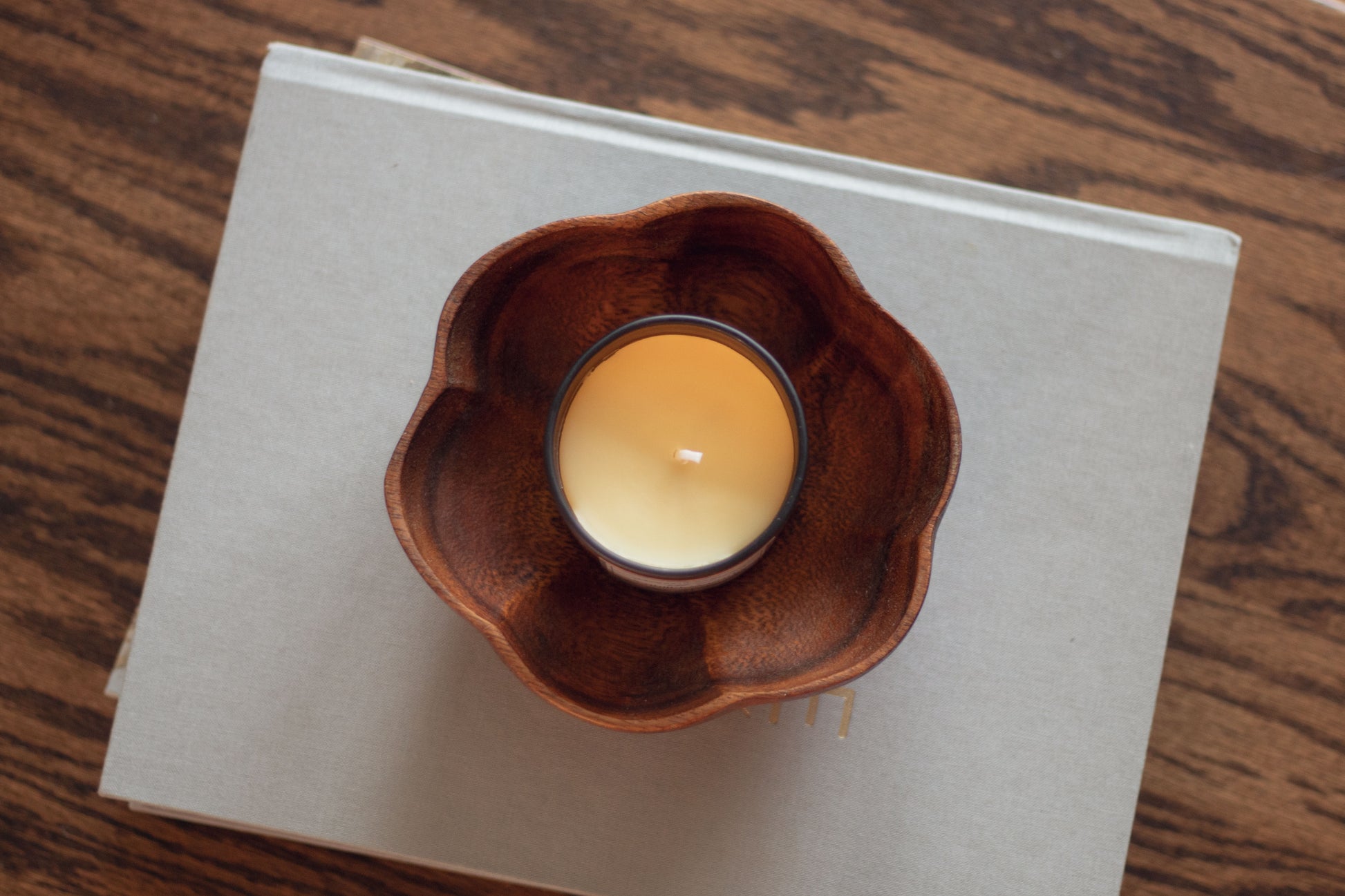 Overhead view of a lit Vanilla Woods candle in a wooden flower-shaped dish on a dark wood table