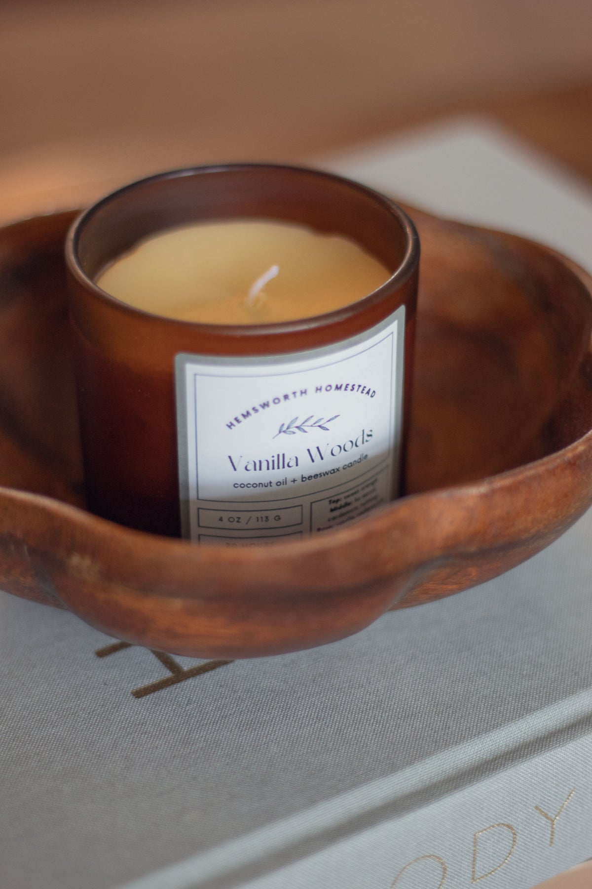 Vanilla Woods candle in a round wooden bowl set on a dark surface