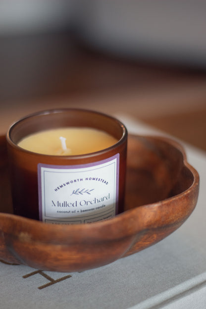 Mulled Orchard candle in a round wooden bowl set on a dark surface