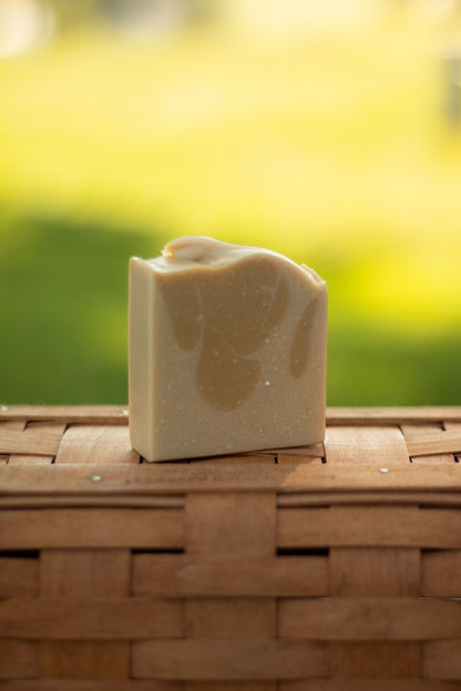 Vanilla Woods bar soap on a wicker basket with a blurred green outdoor background