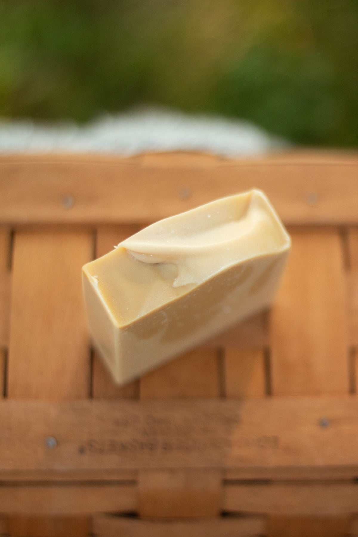 Vanilla Woods bar soap resting on its side on a wicker basket outdoors