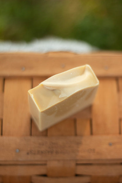 Vanilla Woods bar soap resting on its side on a wicker basket outdoors