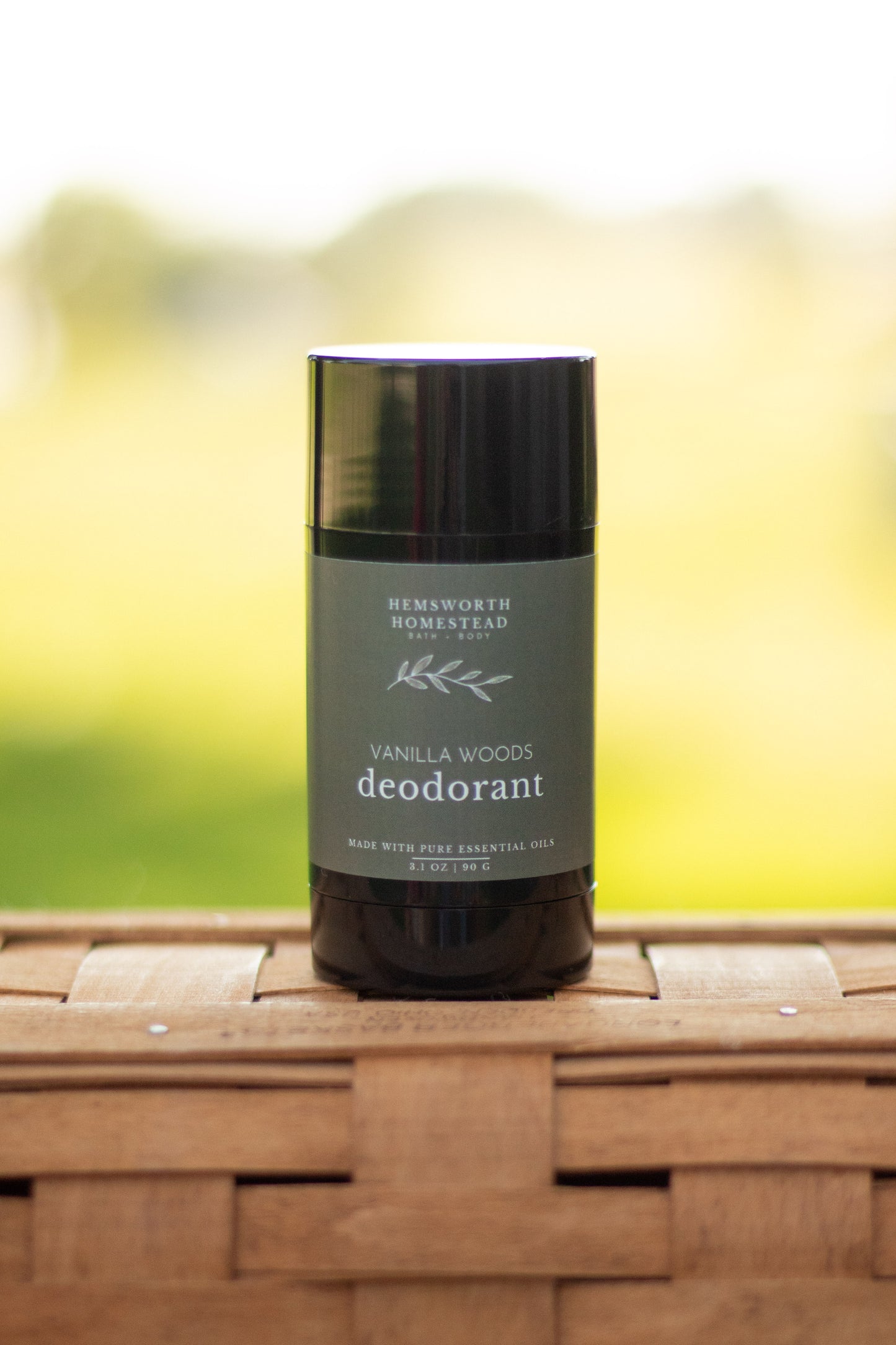 Vanilla Woods deodorant stick standing on a woven basket surface with a blurred green background