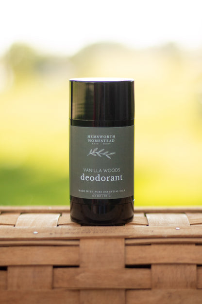 Vanilla Woods deodorant stick standing on a woven basket surface with a blurred green background