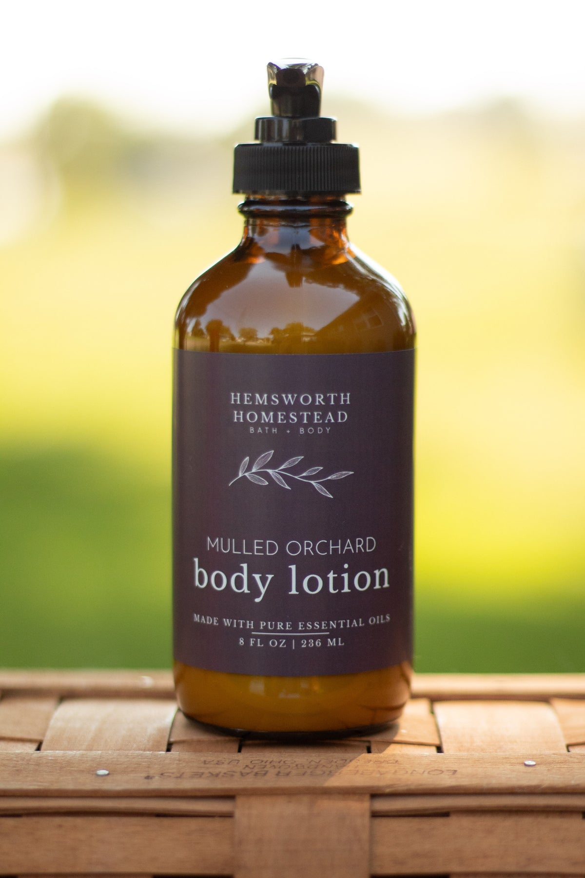 Mulled Orchard body lotion pump bottle on a wicker basket with a blurred green outdoor background