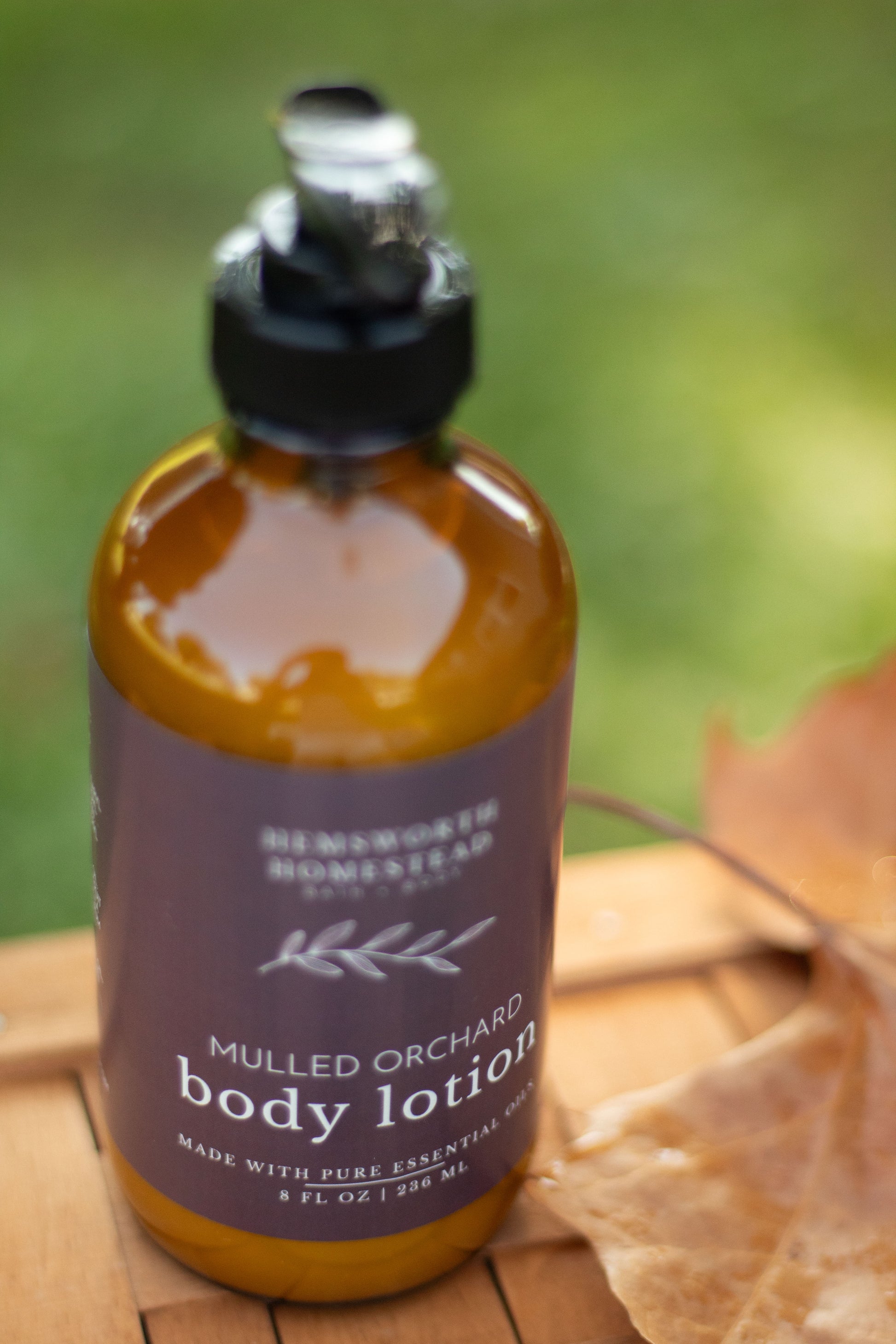 Mulled Orchard body lotion bottle on a wood surface with a dried orange slice, soft green background