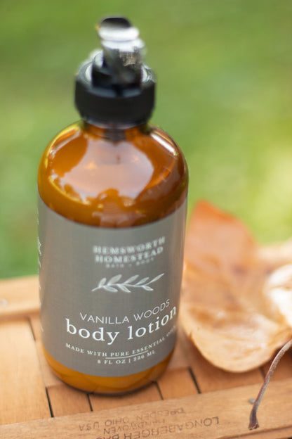Vanilla Woods body lotion bottle on a wood surface with a dried orange slice, soft green background