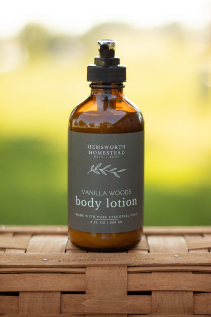 Vanilla Woods body lotion pump bottle on a wicker basket with a blurred green outdoor background