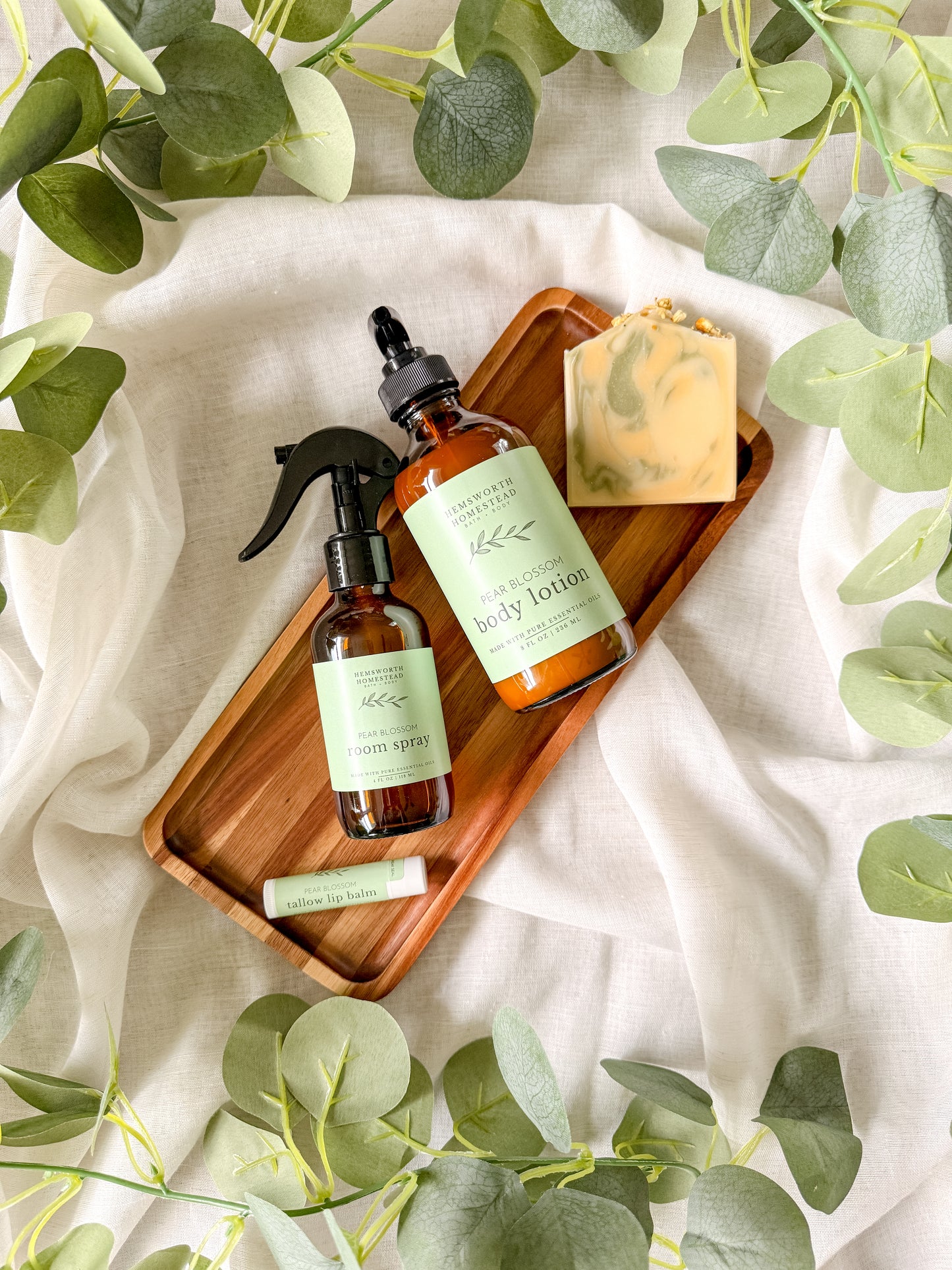 Pear Blossom bundle on a wooden tray - room spray, lotion, swirled bar soap and lip balm, framed by green leaves