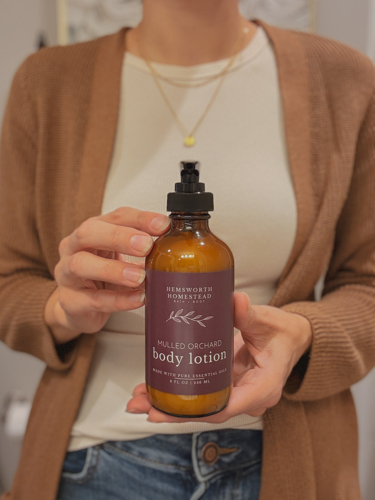 Hands cupping a bottle of Mulled Orchard body lotion, soft neutral background