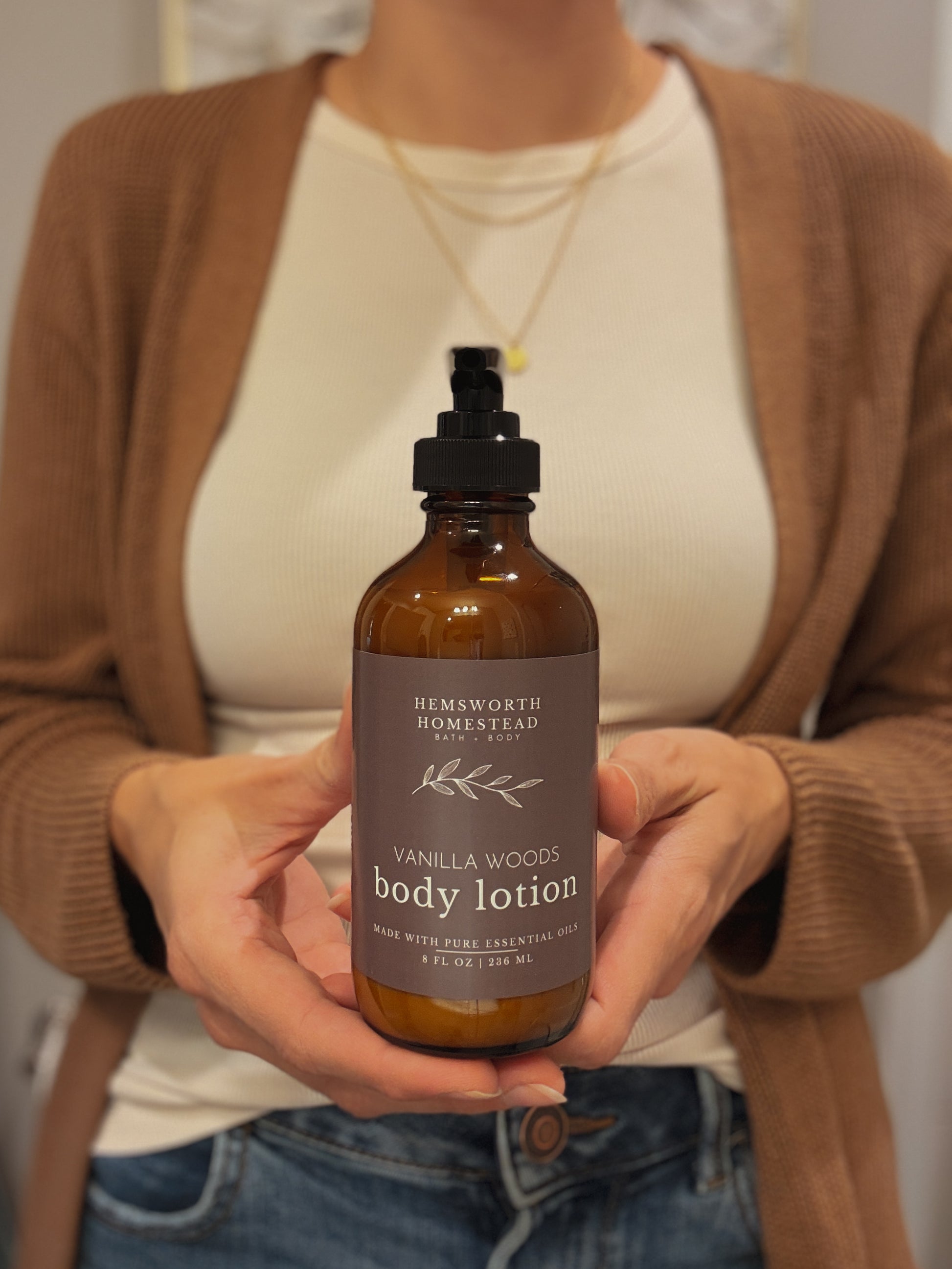 Hands cupping a bottle of Vanilla Woods body lotion, soft neutral background